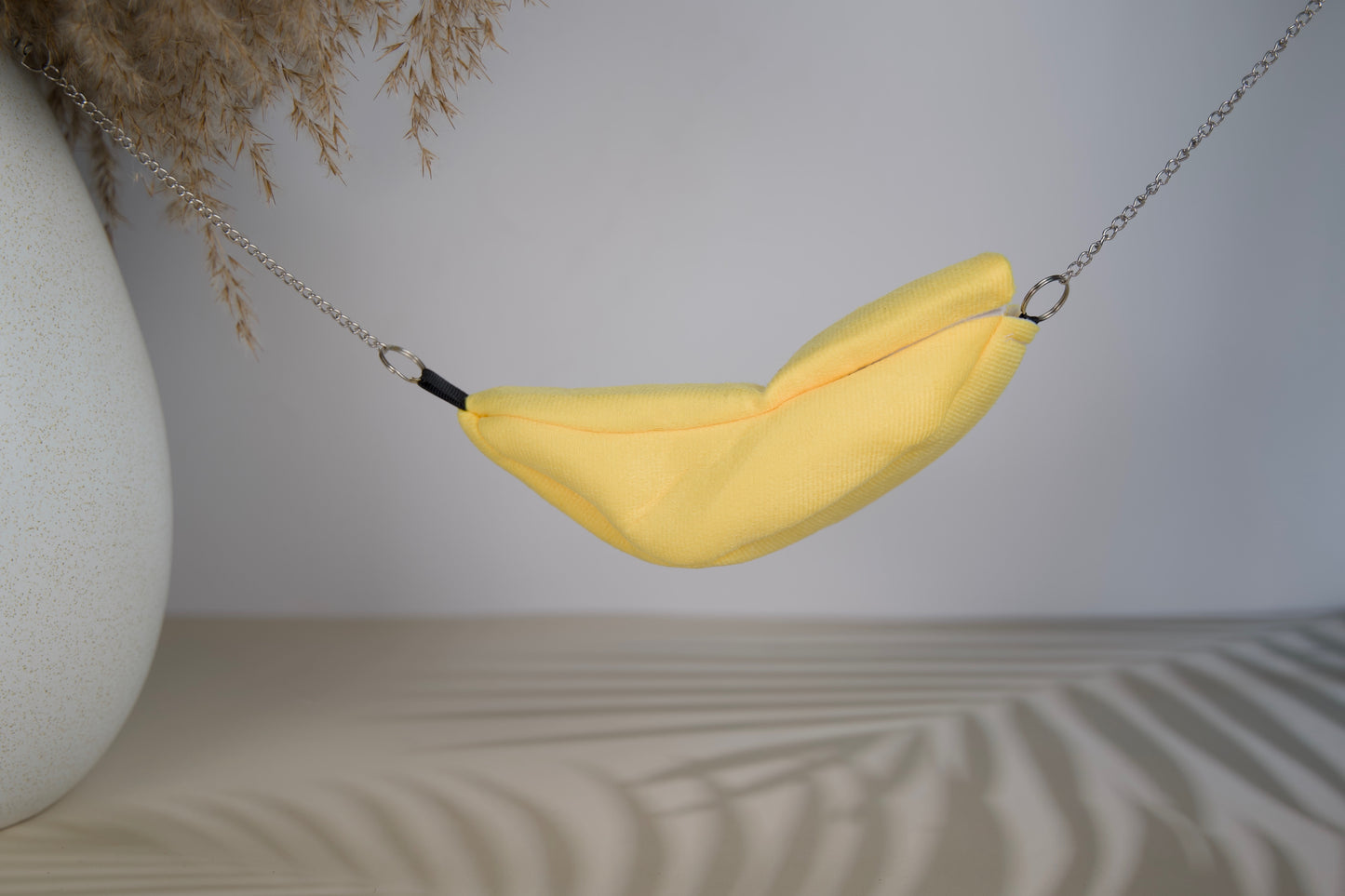 Yellow fabric hammock shaped like a banana for hasmters on a neutral background.