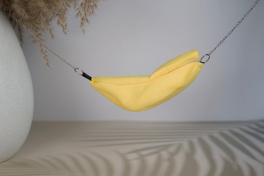 Yellow fabric hammock shaped like a banana for hasmters on a neutral background.|Hamac en tissu jaune en forme de banane pour hamsters sur fond neutre.