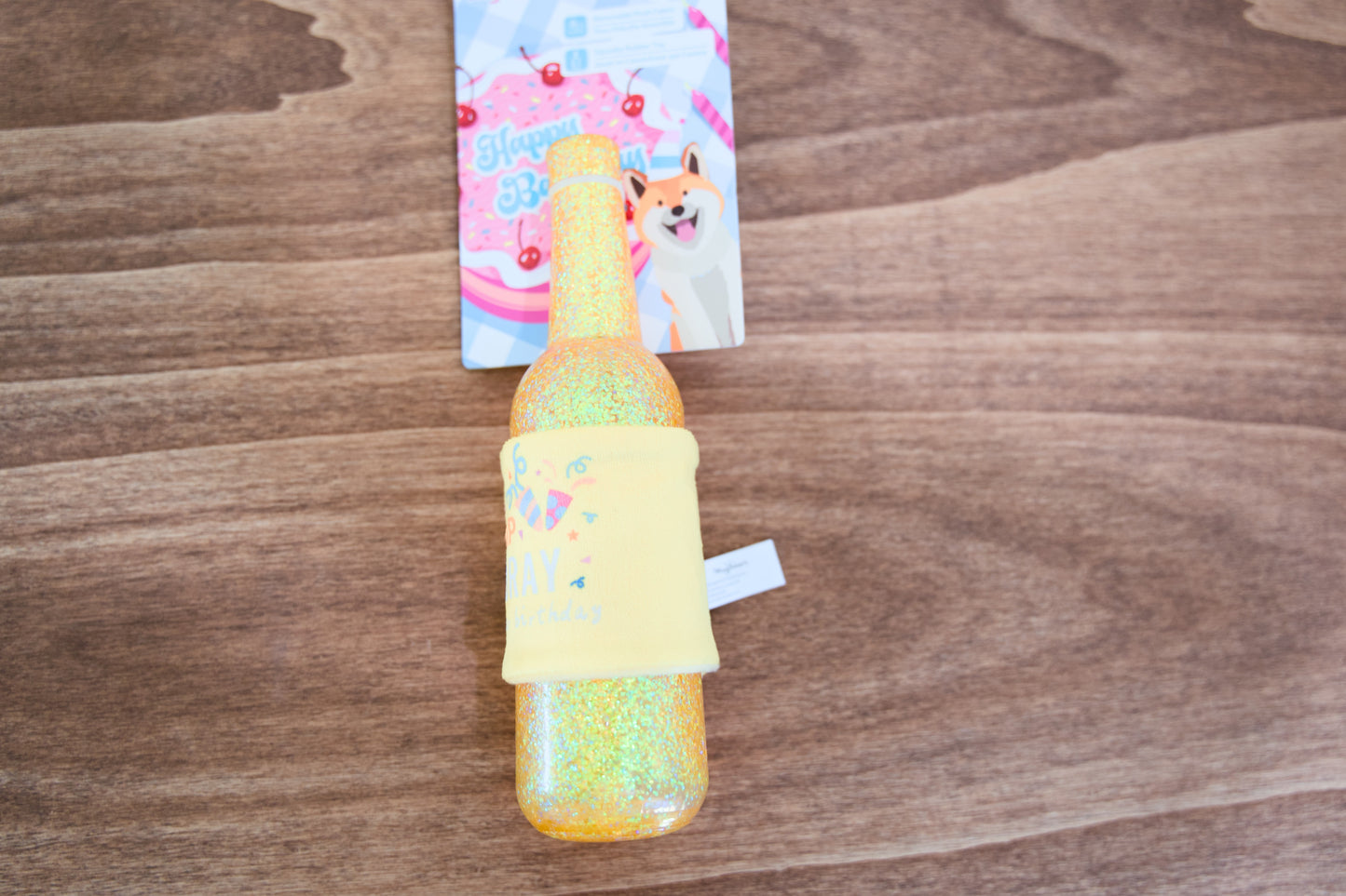 Colorful glittery bottle-shaped toy on a wooden surface with a colorful dog toy in the background.