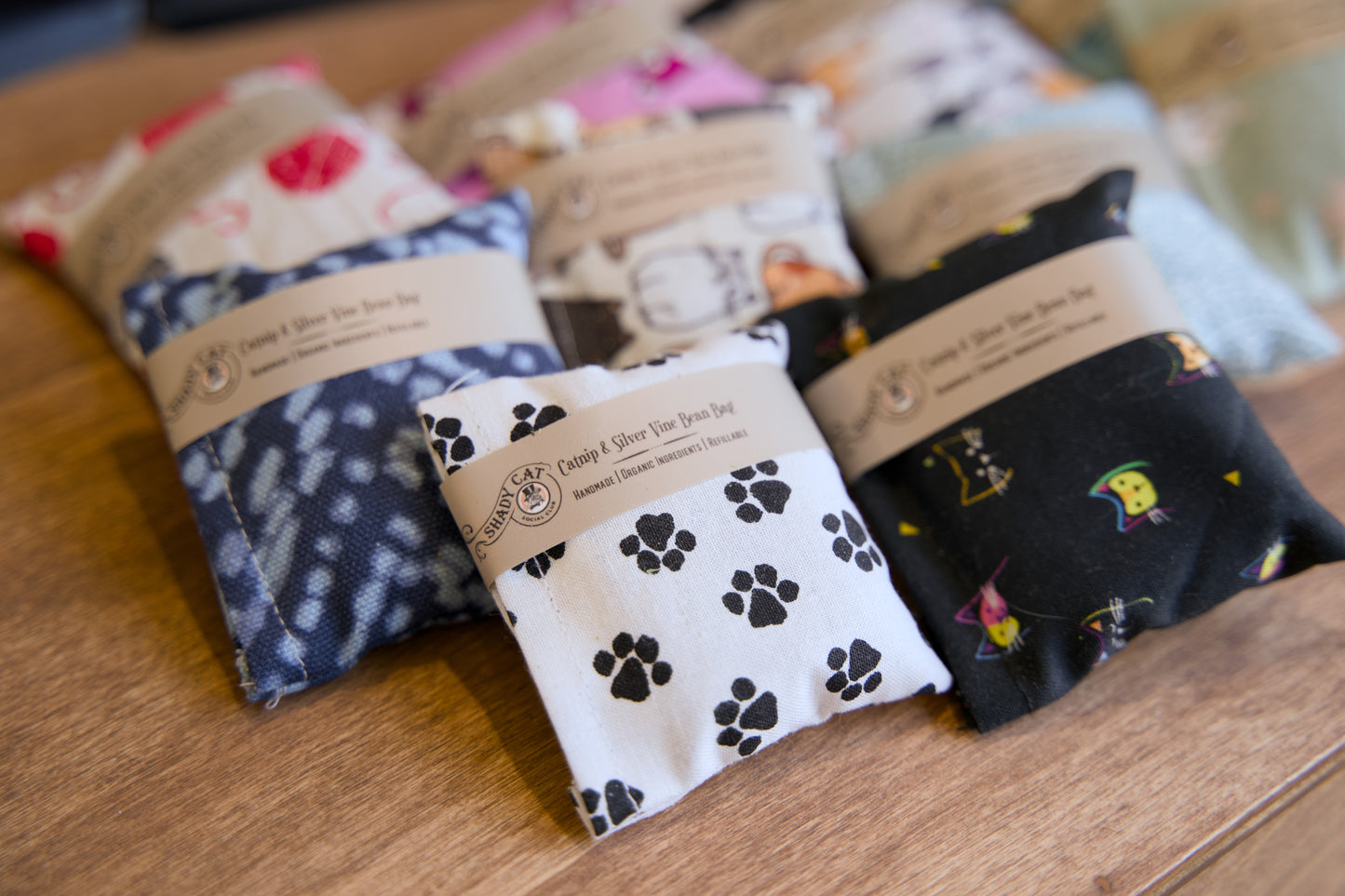 Quatre coussins remplis d'herbe à chat et de vigne argentée pour chats, avec différents motifs, posés sur une surface en bois.