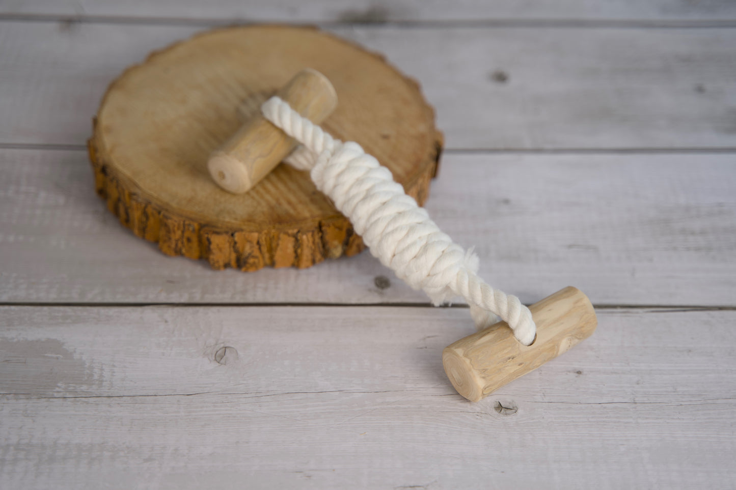 Jouet en bois pour chien avec une corde en coton, posé sur une surface en bois.