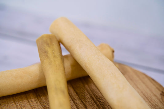 Close-up view of the three cow tail sticks for dogs on a round wooden board.|Vue en gros plan des trois bâtonnets de queue de bœuf pour chiens sur une planche en bois ronde.