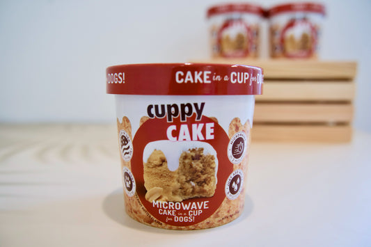 Cuppy Cake peanut butter flavor microwave cake for dogs on a light surface with a neutral background.|Gâteau pour chiens Cuppy Cake (saveur beurre de cacahuète), préparable au micro-ondes, posé sur une surface claire avec un arrière-plan neutre.