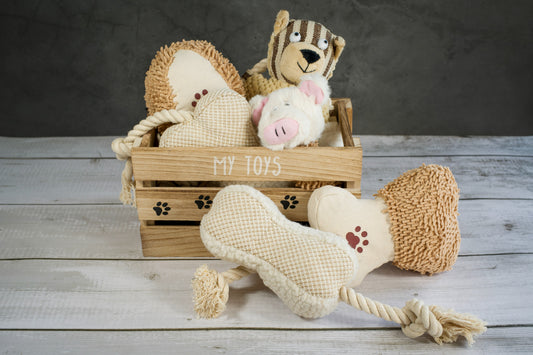 Wooden basket with neutral colored plush and rope toys for dogs. | Panier en bois avec jouets en peluche pour chiens.