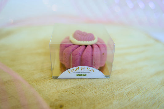 Pink dog treat made with sardine in a clear box on a wooden surface with Pearl & Park branding.|Friandise rose pour chien à base de sardines, présentée dans une boîte transparente sur une surface en bois, avec la marque Pearl & Park.
