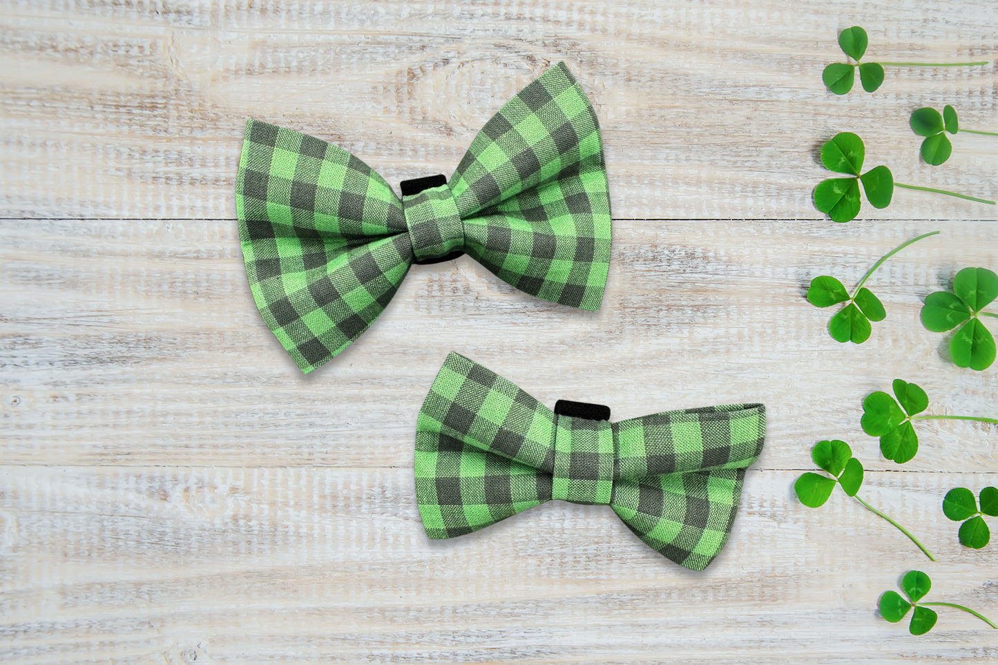 Two green and black checkered dog bow ties on a wooden surface with clover leaves.
