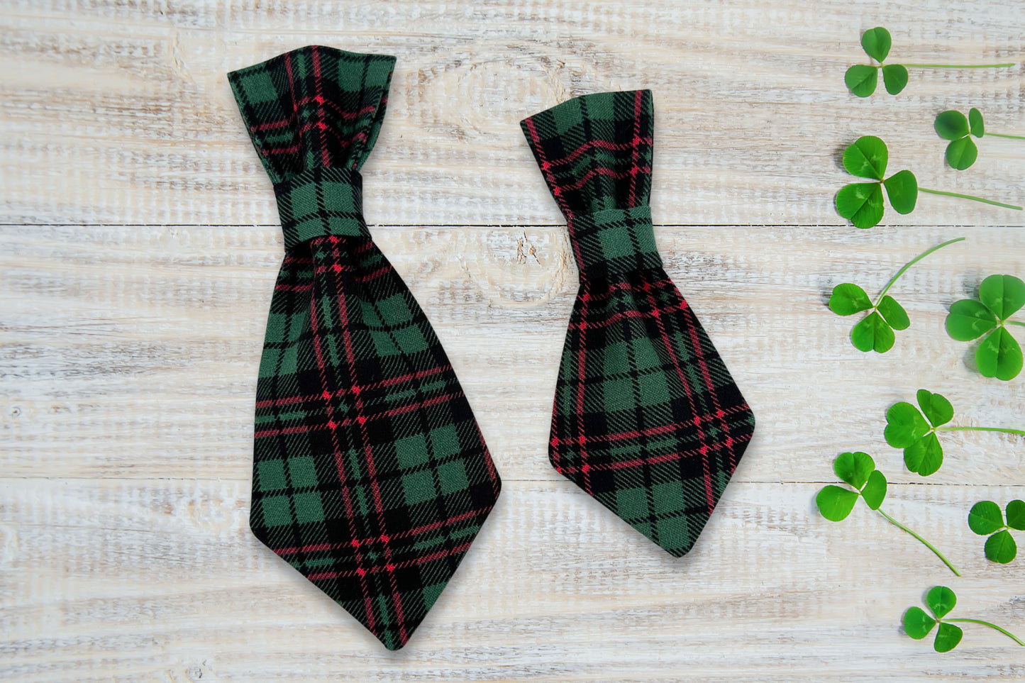 Two green plaid dog ties on a wooden surface with clover leaves.