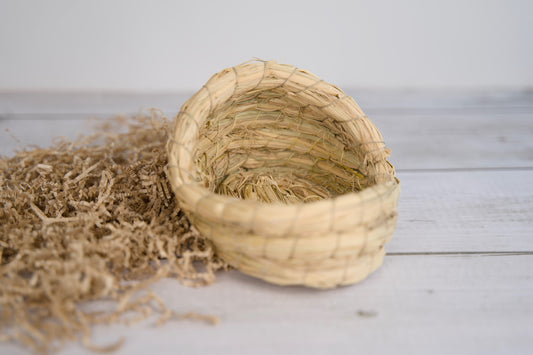 Woven small pet basket with straw-like material on a light wooden surface.|Panier tressé pour hamster en matière semblable à de la paille, posé sur une surface en bois clair.