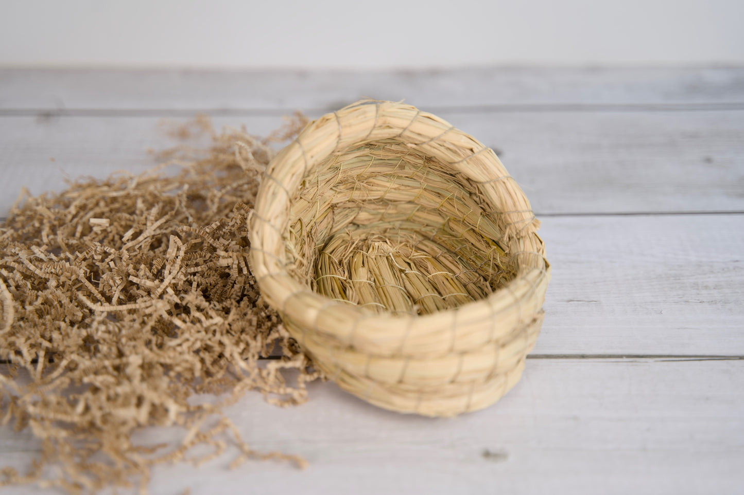 Panier en paille tressée pour petits animaux, posé sur une surface en bois.