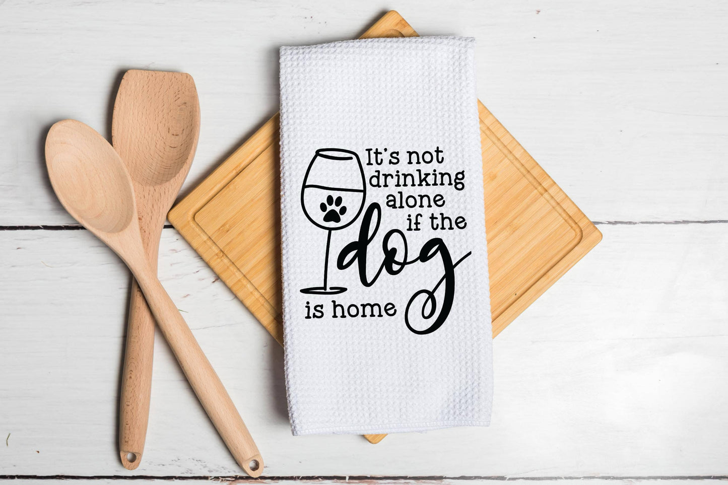 Dog-themed kitchen towel with humorous text on a wooden surface with utensils.