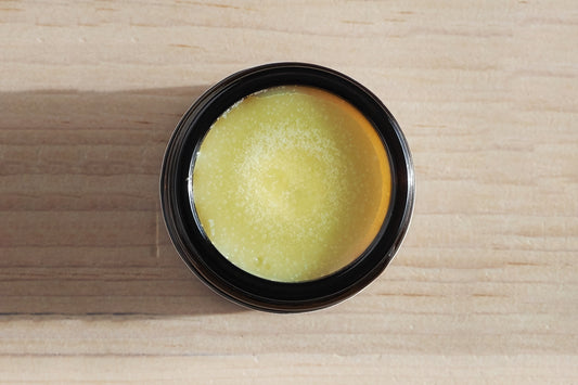 Dog nose balm in a black container on a wooden surface.|Baume pour le nez du chien dans un récipient noir sur une surface en bois.