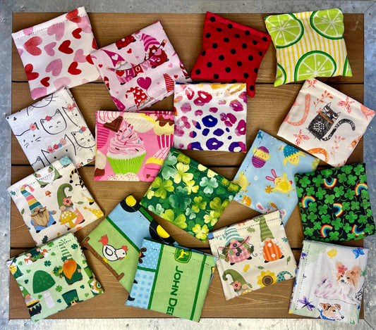 Collection of colorful fabric squares cat kickers with various patterns on a wooden surface.|Collection de jouets pour chats en forme de carrés de tissu colorés avec différents motifs, posés sur une surface en bois.