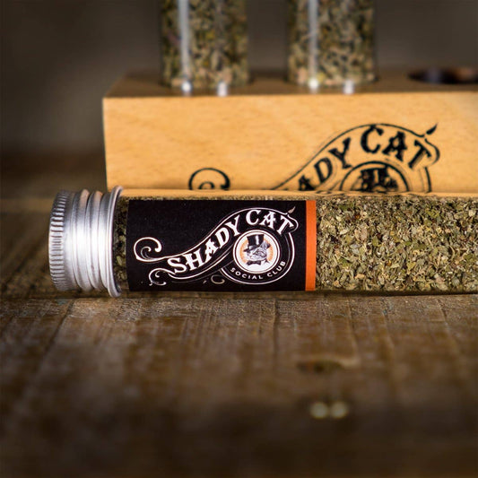 Shady Cat Social Club leaf flower and catnip product packaging on a wooden surface.|Emballages de produits Shady Cat Social Club (feuilles, fleurs et herbe à chat) sur une surface en bois.