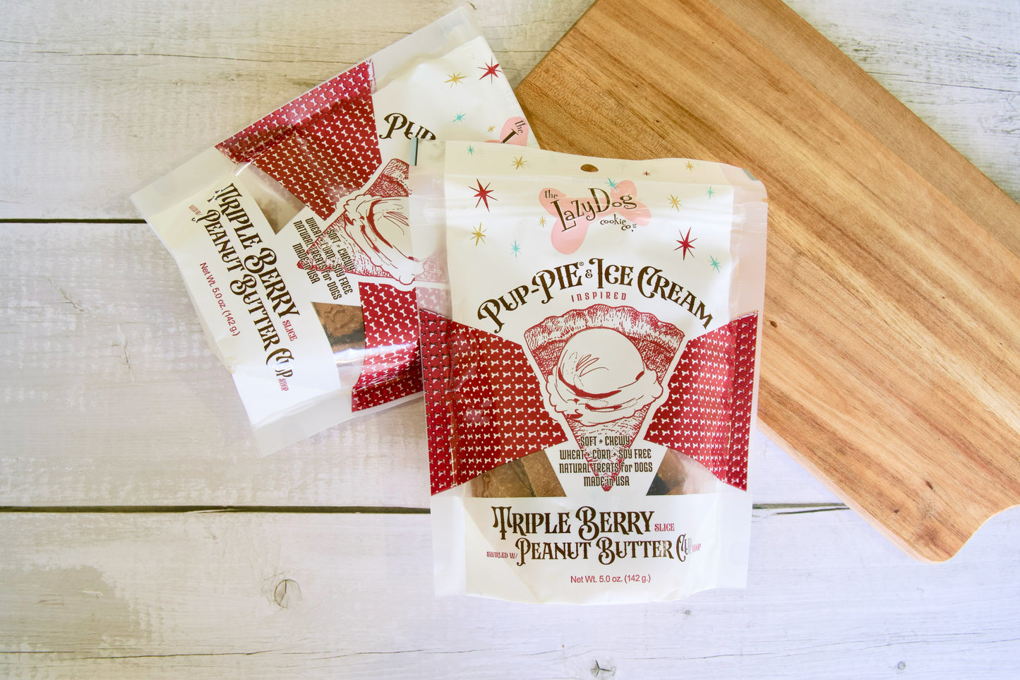 Packages of dog treats: triple berry peanut butter from Pup Pie Ice Cream on a wooden surface.