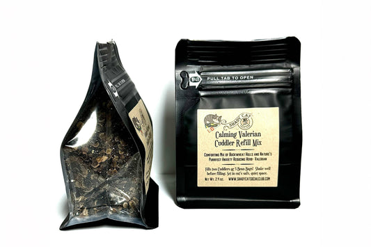 Two black resealable bags of Calming Valerian Cuddler Refill Mix on a white background, one showing the loose herbal blend through a clear window and the other showing the front label.|Deux sachets noirs refermables de mélange de recharge « Calming Valerian Cuddler » sur fond blanc : l'un laisse entrevoir le mélange de plantes en vrac à travers une fenêtre transparente, tandis que l'autre présente l'étiquette avant.