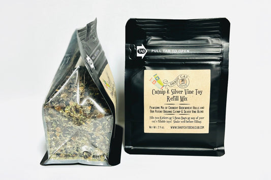 Two product pouches on a plain white background: a clear stand-up bag filled with loose dried herbs and a black resealable pouch labeled 'Catnip & Silver Vine Toy Refill Mix' with a beige front label.|Deux sachets de produits sur fond blanc uni : un sachet transparent à fond plat contenant des herbes séchées en vrac et un sachet noir refermable portant l'étiquette « Catnip & Silver Vine Toy Refill Mix » et une étiquette frontale beige.
