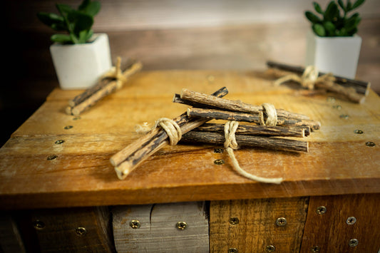 Stack of cat sticks tied together on a wooden surface with plants in the background.|Pile de bâtonnets pour chats attachés ensemble sur une surface en bois, avec des plantes en arrière-plan.