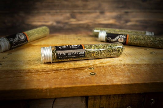 Tube of catnip and silver vine on a wooden surface with other similar tubes in the background.|Un tube d'herbe à chat et de vigne argentée posé sur une surface en bois, avec d'autres tubes similaires en arrière-plan.