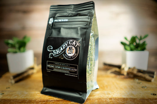 Shady Cat catnip and silvervine bag on a wooden surface with plants in the background.|Sac d'herbe à chat et vigne argentée de la marque Shady Cat posé sur une surface en bois, avec des plantes en arrière-plan.