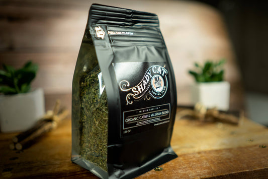 A bag of Shady Cat catnip for cats is placed on a wooden surface with a blurred background.|Un sac de catnip pour chats de Shady Cat posé sur une surface en bois avec un arrière-plan flou.