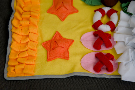 Close-up of a handmade snuffle mat with palm tree and seashell designs, crafted for pet enrichment.|Gros plan sur un tapis de fouille fait main avec des motifs de palmier et de coquillage, conçu pour la stimulation des animaux.