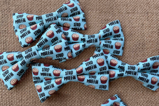 Multiple dog and cats bow ties with stud muffin pattern on a textured fabric background.|Lot de nœuds papillon pour chiens et chats, à motif Stud Muffin sur fond en tissu texturé.