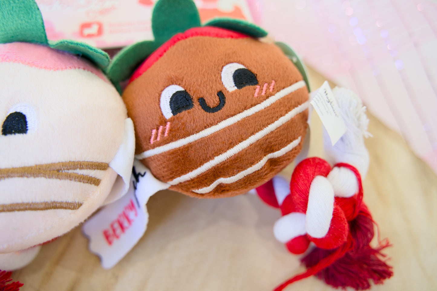 Rope dog toy resembling a cookie with a face, surrounded by other plush toys on a light background.