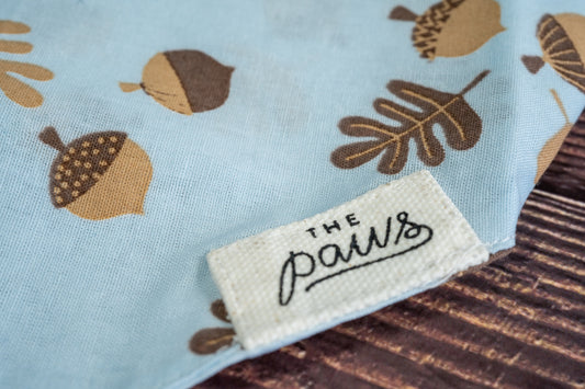 Close-up of The Paws logo on the light blue dog bandana. | Gros plan sur le logo The Paws sur le bandana pour chien bleu clair.
