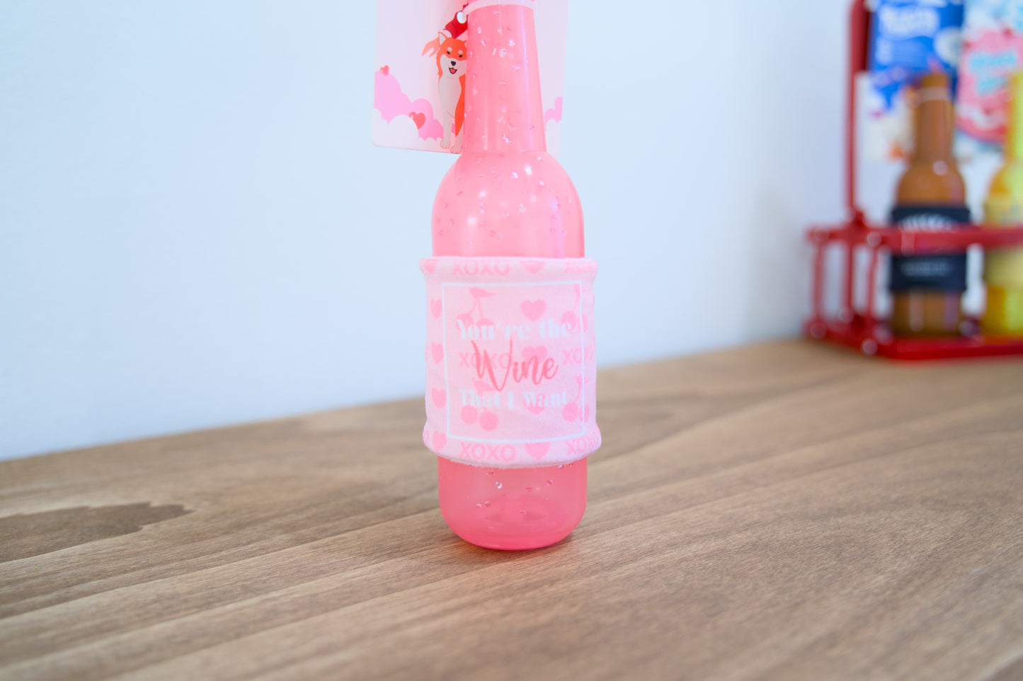 Pink bottle valentines dog toy on a wooden surface.