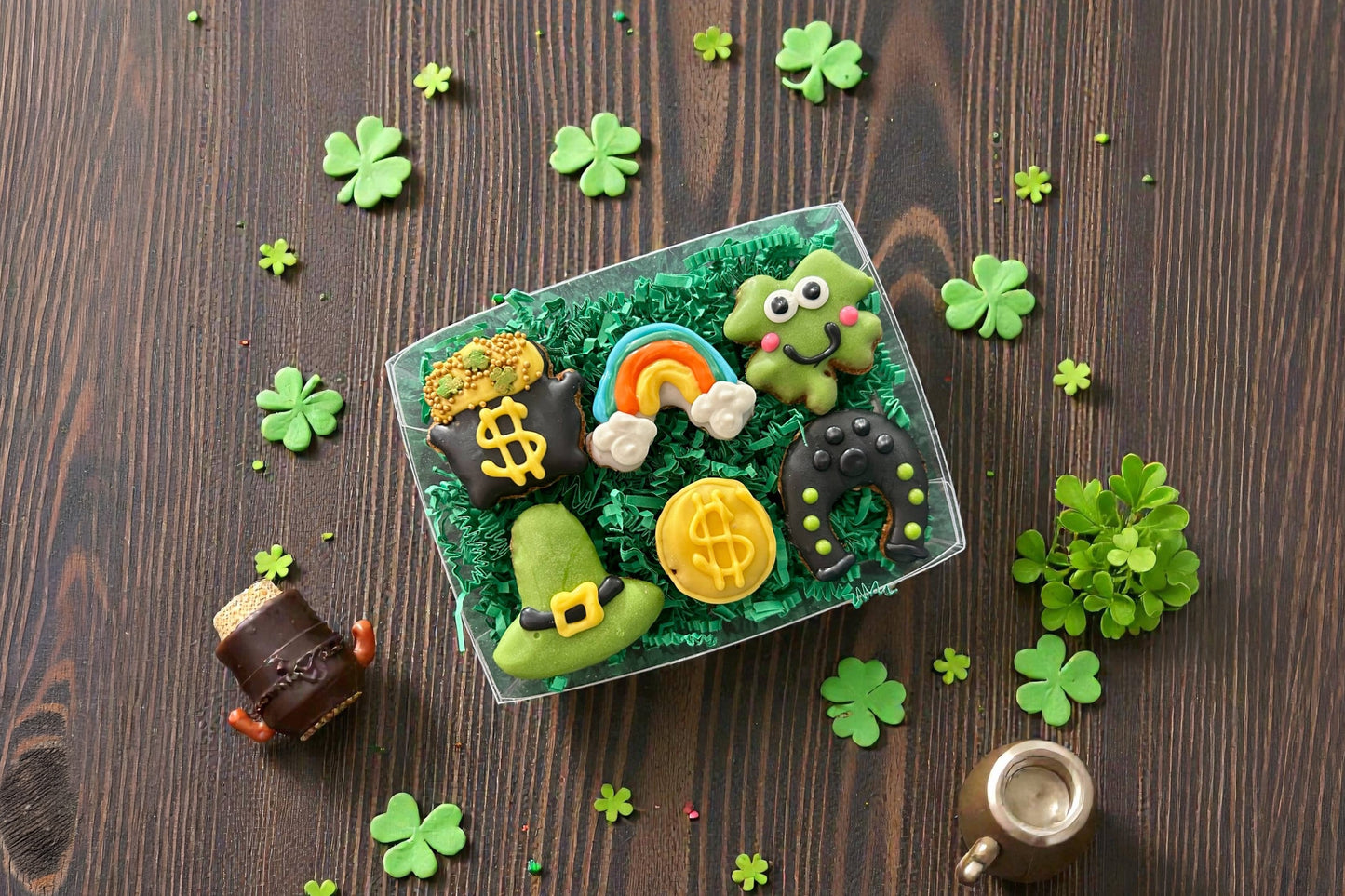 Decorative dog cookies with green icing, gold coins, a rainbow, and shamrocks on a wooden surface.