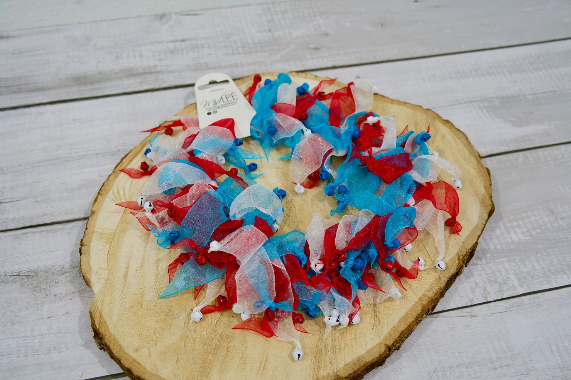 Rubans rouges, blancs et bleus avec des grelots pour colliers d'animaux, disposés sur une planche en bois.
