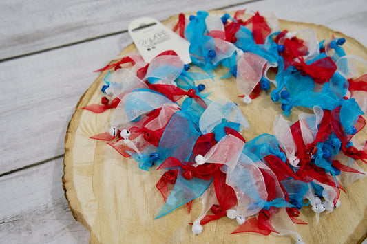 Decorative pet collar with red, white, and blue ribbons on a wooden surface.|Collier décoratif pour animal avec des rubans rouges, blancs et bleus, posé sur une surface en bois.