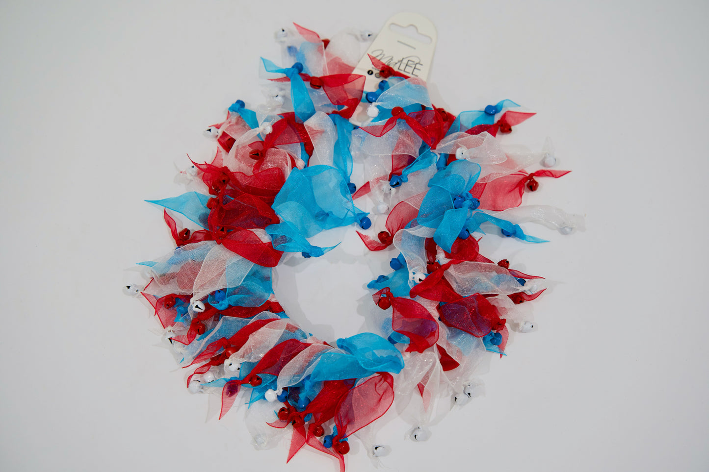 Collier décoratif pour animal avec des rubans et des grelots rouges, blancs et bleus sur fond blanc.