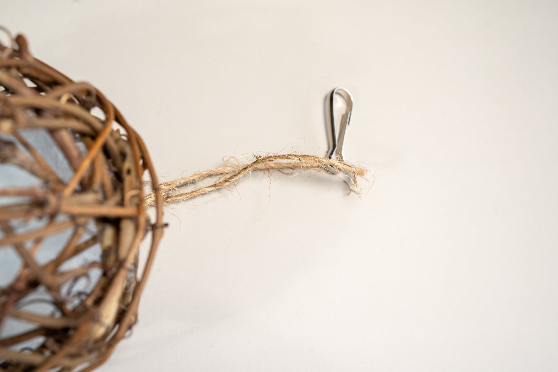 Close-up view of the rope and hook for hanging the rattan bird ball. | Vue rapprochée de la corde et du crochet pour accrocher la balle en branches de vigne pour oiseaux.