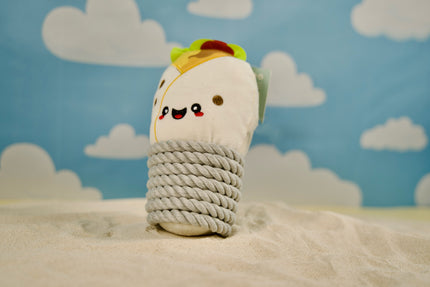 Dog toy shaped like a burrito resting on a sandy beach.
