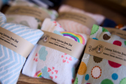 Des coussins colorés remplis de valériane pour chats, avec des étiquettes, posés sur une surface en bois.