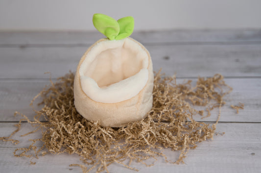 Small boat-shaped plush hideout with a green leaf on top, placed on a bed of brown seaweed.|Petite cachette en peluche en forme de bateau, surmontée d'une feuille verte, posée sur un lit d'algues brunes.