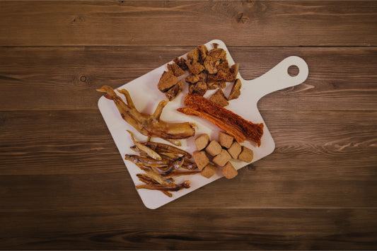 Assorted freeze-dried meats and snacks for dogs on a charcuterie board.|Un assortiment de viandes et de friandises lyophilisées pour chiens, présenté sur une planche de charcuterie.