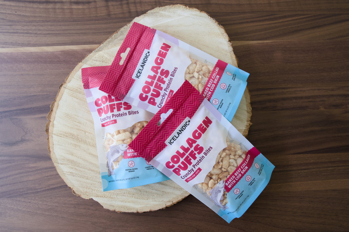 Trois sachets de friandises pour chats Icelandic+ Collagen Puffs sur une planche en bois.