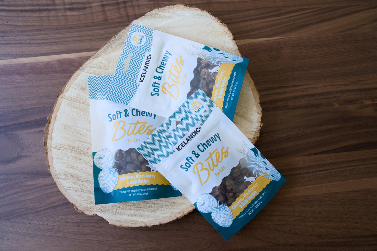 Trois paquets de bouchées au poulet Icelandic+ tendres et moelleuses pour chats, présentés sur une rondelle de bois.