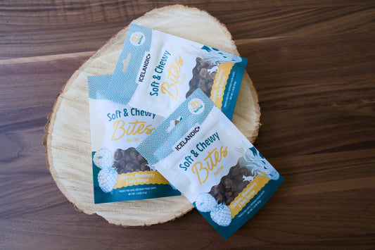 Three packages of Icelandic+ soft & chewy chicken bites for cats on a round wood slice.|Trois paquets de bouchées au poulet Icelandic+ tendres et moelleuses pour chats, présentés sur une rondelle de bois.