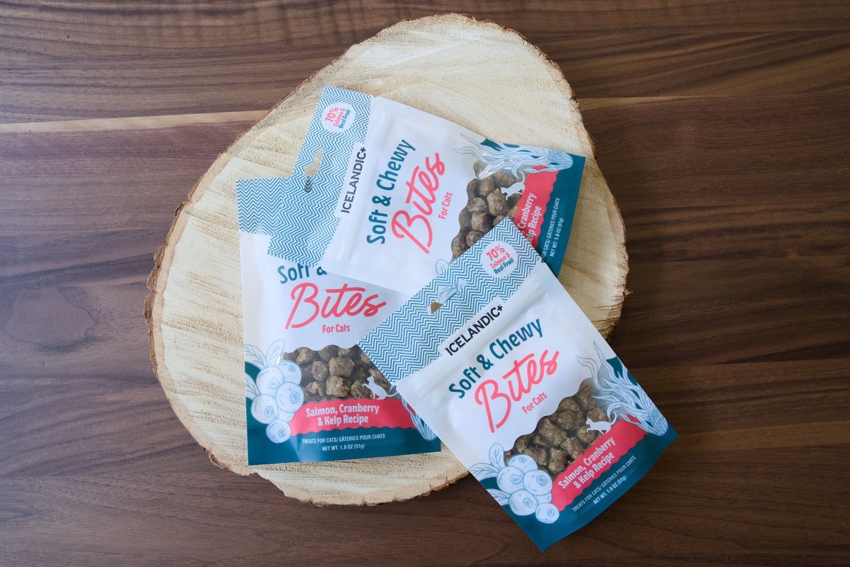 Trois sachets de friandises pour chats tendres et moeilleuses Icelandic+ posés sur une planche de bois.