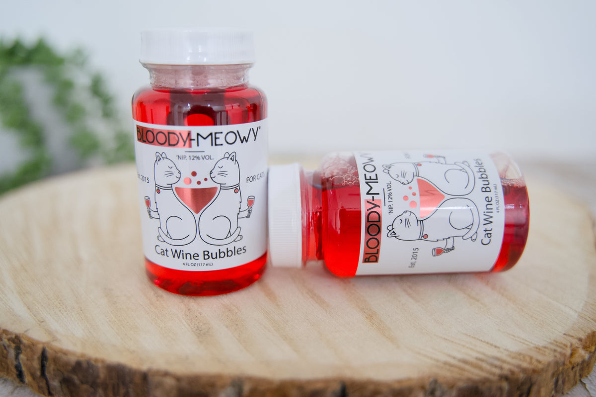 Two bottles of Bloody-Meowy cat wine bubbles on a wooden surface with a blurred background.