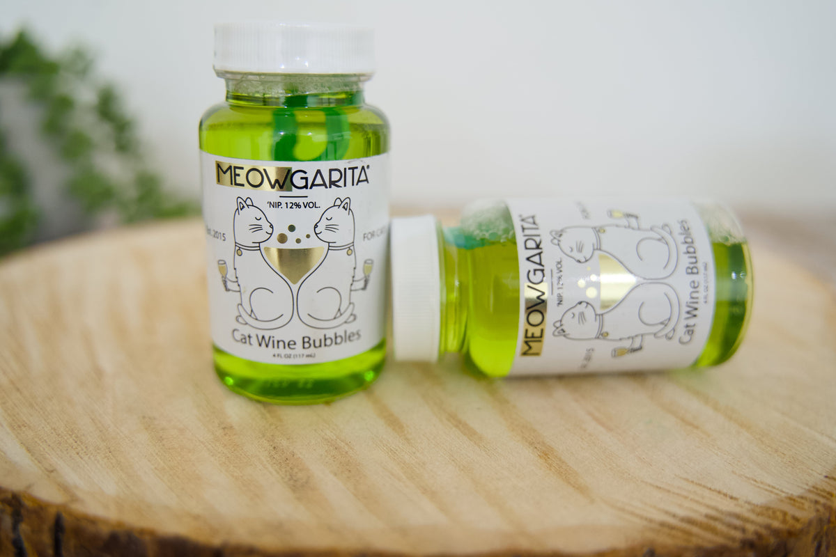 Two bottles of Meowgarita cat wine bubbles on a wooden surface with a blurred background.