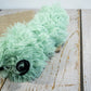 Side view of green cat plush toy in the shape of a caterpillar and filled with catnip.