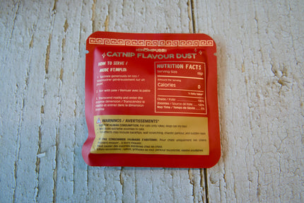 Un sachet rouge de poudre aromatisée à l'herbe à chat pour félins, posé sur une surface en bois blanc patiné par le temps.