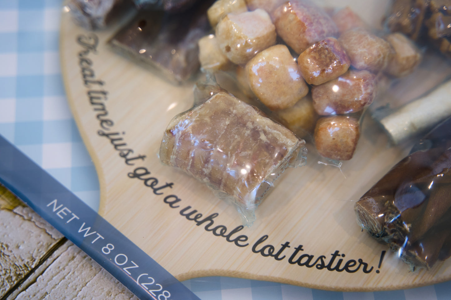 Assorted candies for dogs on a wooden board with text, on a checkered tablecloth.