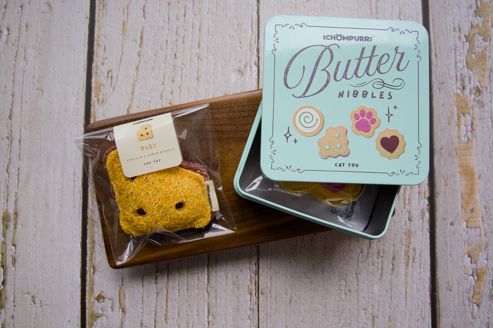 A cat toy duet cookie on a wooden tray next to its mint green tin box labeled Butter Nibbles.