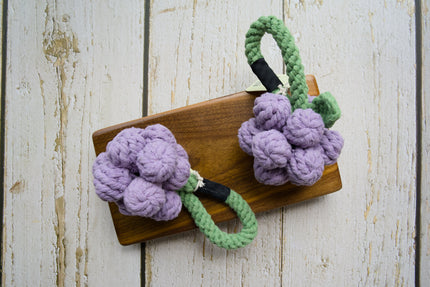 Two woven cotton grape clusters with green rope stems for dogs on a wooden board.