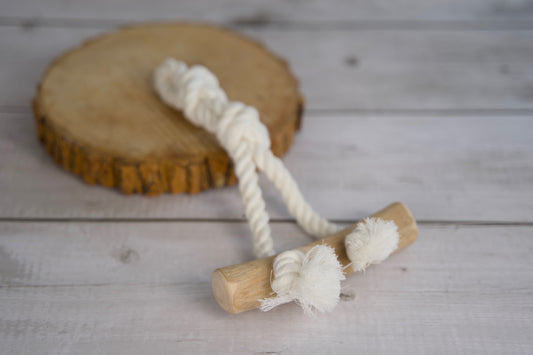 Dog toy with rope and wooden piece on a wooden surface.|Jouet pour chien avec corde et pièce en bois, posé sur une surface en bois.